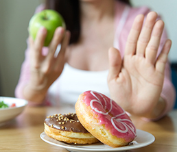 Young girl rejecting junk food or unhealthy food such as donuts and choosing healthy food such as a green apple and salad for having a good health. Dieting and good health concept.